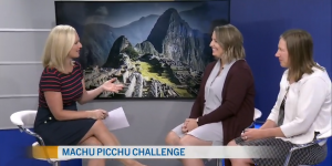 A woman interviewing two other people with a photo of Machu Picchu in the background
