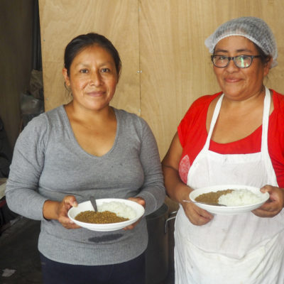 Two Peruvian woman smiling at the camera and holding plates of food
