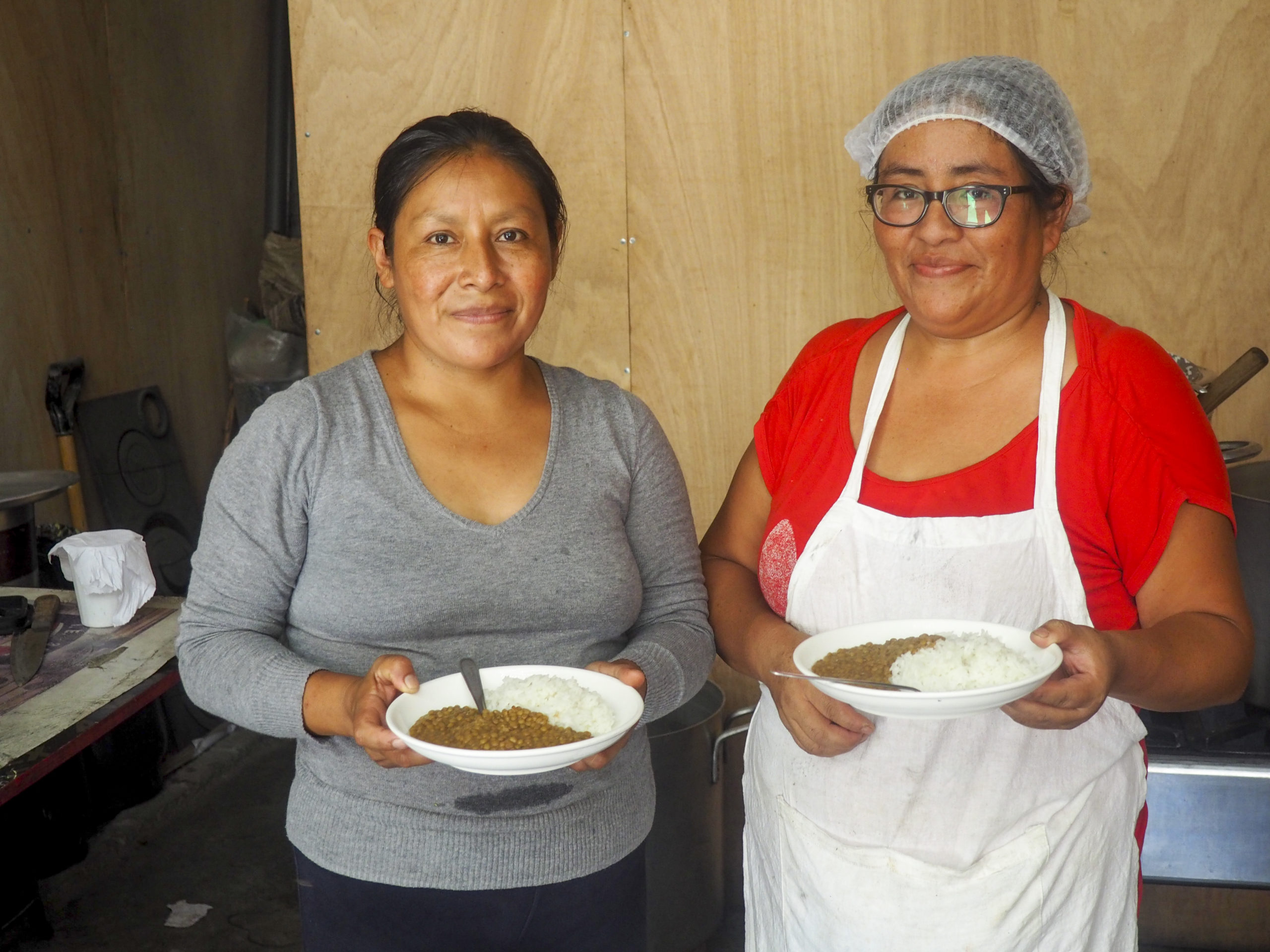 Two Peruvian woman smiling at the camera and holding plates of food