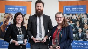 Three people holding award plaques smiling at camera