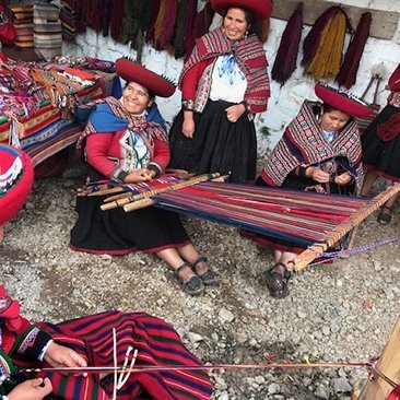 Women in traditional clothing weaving a rug