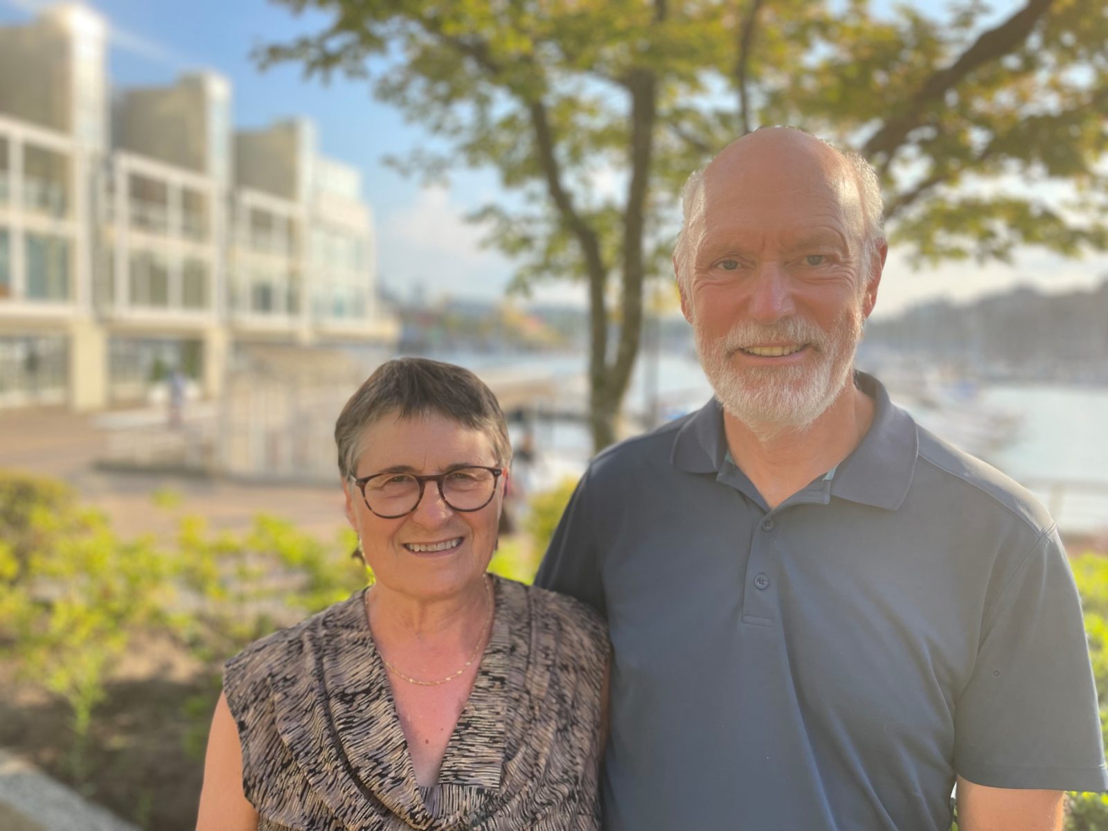 Two older people, a man and woman, smiling in the sun at the camera