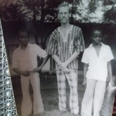 A black and white image of Richard standing with two boys in white shirts