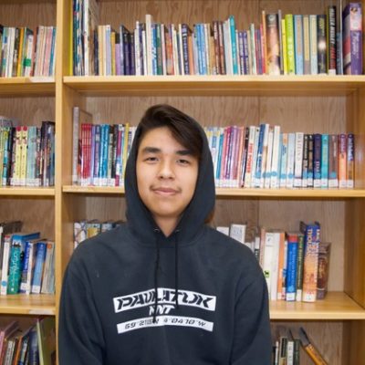 A young man in a hoodie standing in front of a book shelf