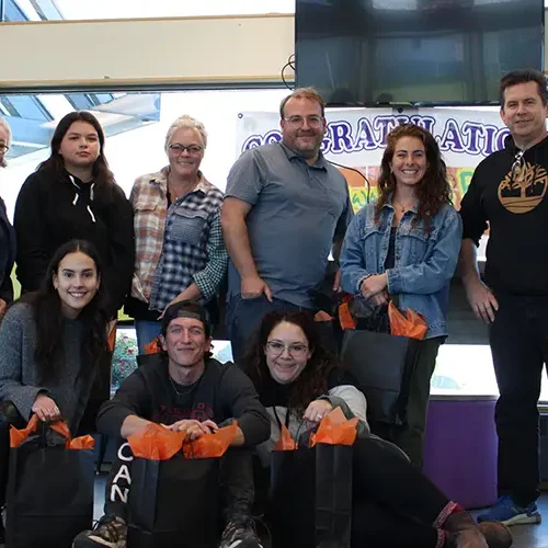 A group of eight people smiling indoors, holding gift bags in the Northwest Territories, with a congratulatory banner.