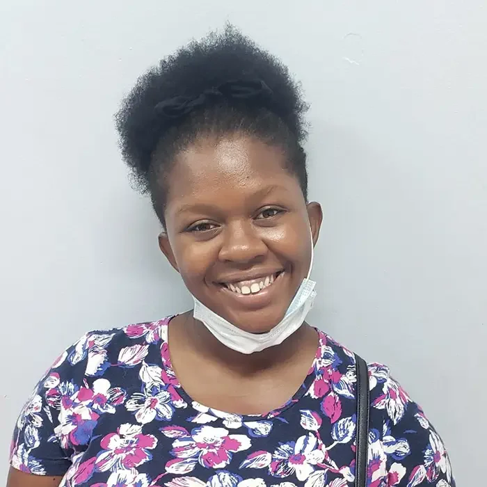 A smiling person with natural hair dons a floral shirt and a chin mask, inspired by Cuso International in the Caribbean.