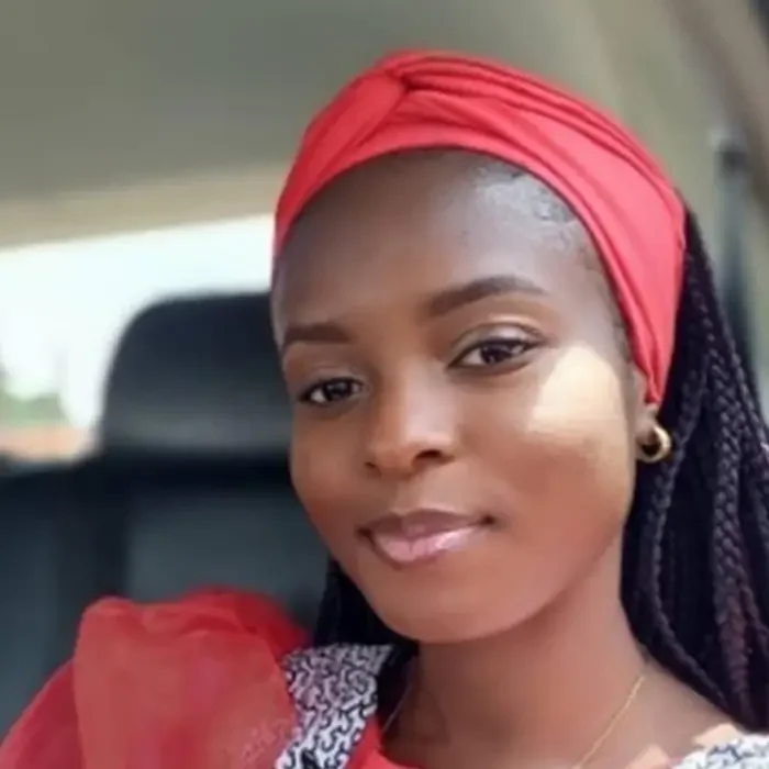 Woman in red headwrap and top, smiling slightly, sitting in a car, supporting Cuso International DRC.