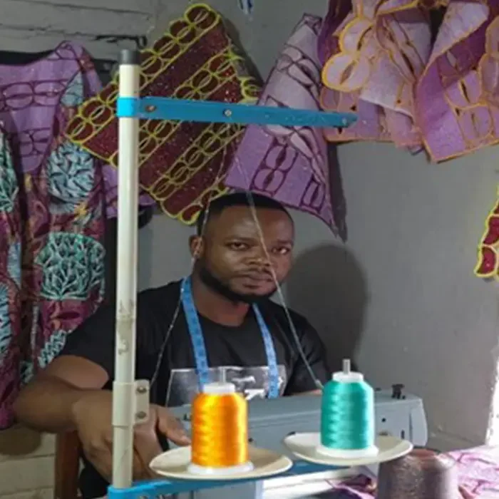 A man sewing with a Cuso International machine, surrounded by vibrant fabrics and spools of thread in DRC.