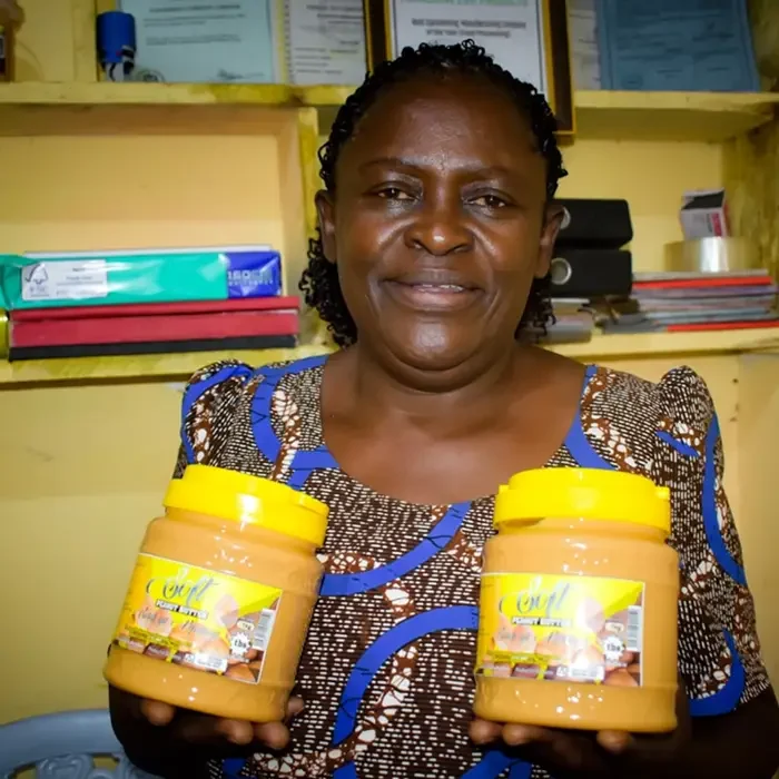 A person smiling and holding two jars of peanut butter at Cuso International's Tanzania office.