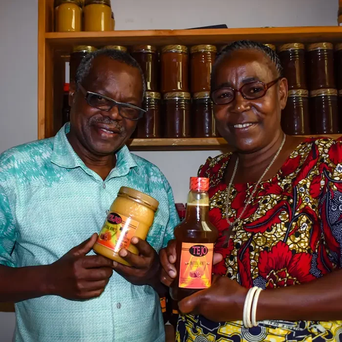 Two people smiling, holding "Tej" bottles in a shop, reminiscent of Cuso International Tanzania's vibrant markets.