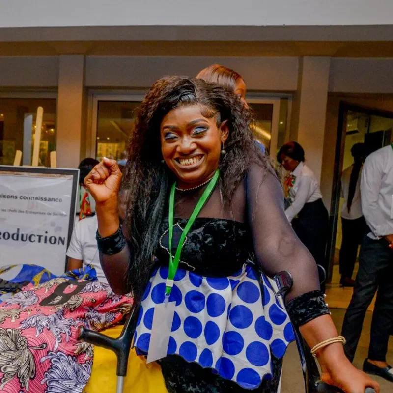 Woman smiling and posing beside a display of colourful textiles at a community event in the DRC / Femme souriante posant à côté d’un présentoir de textiles colorés lors d’un événement communautaire en RDC