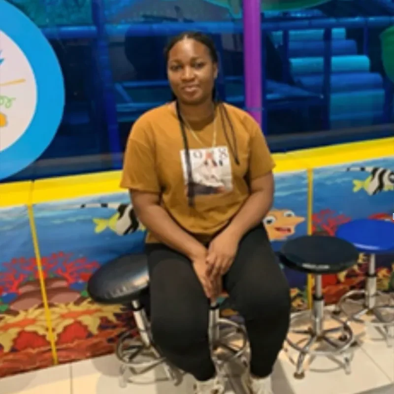 Young woman seated on a stool in a brightly coloured indoor community space in the Democratic Republic of Congo / Jeune femme assise sur un tabouret dans un espace communautaire intérieur aux couleurs vives en République démocratique du Congo