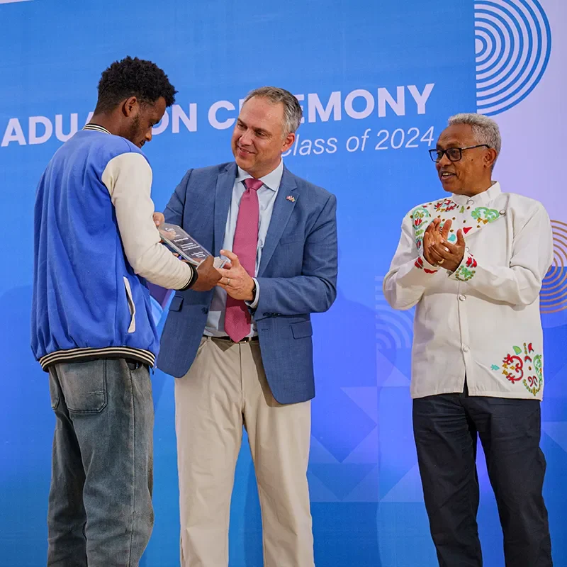 Diplômée en toge bleue recevant un certificat d’un présentateur sur scène, tous deux souriants