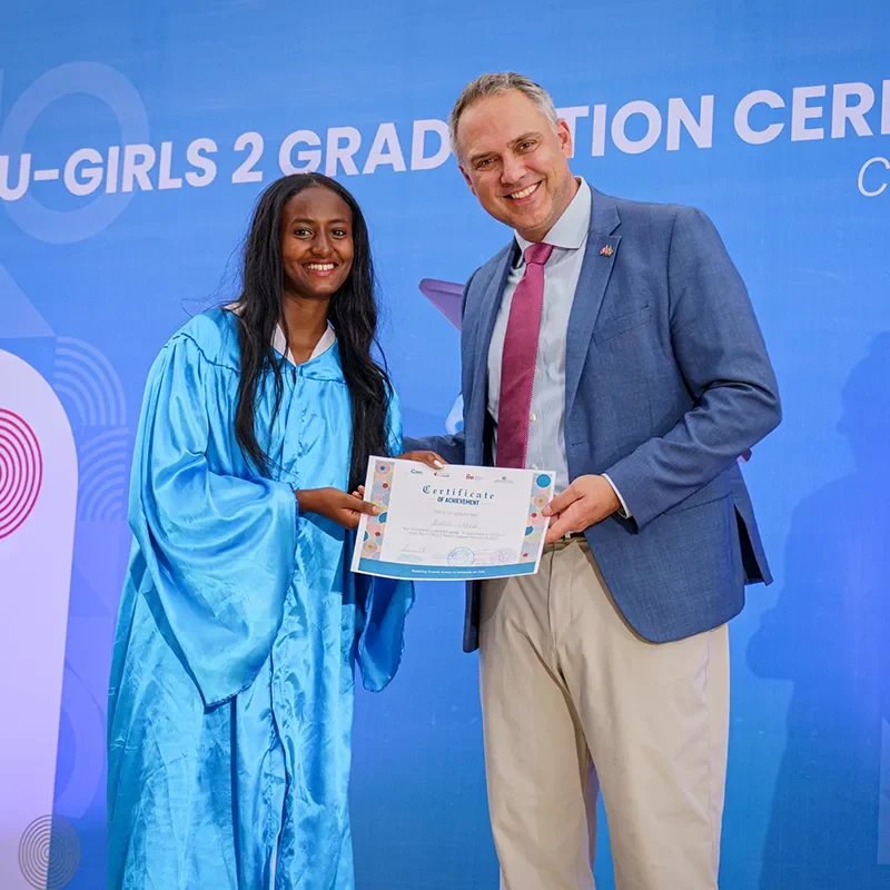 Diplômée en toge bleue recevant un certificat d’un présentateur sur scène, tous deux souriants