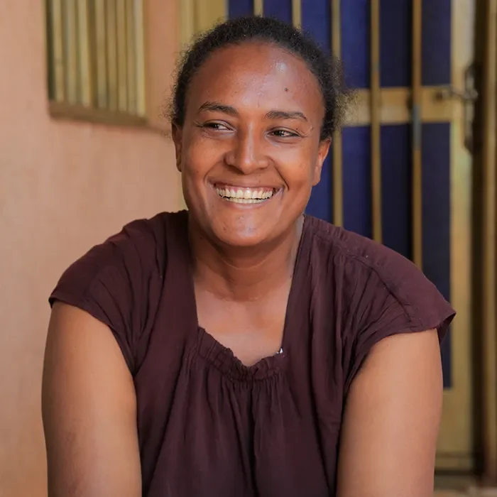 Femme souriante assise à l’intérieur, regardant directement la caméra
