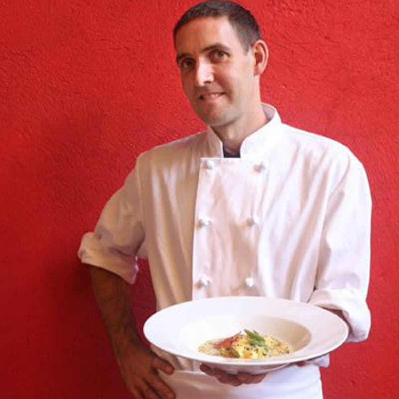 Bryan holding a plate with pasta in front of a red wall