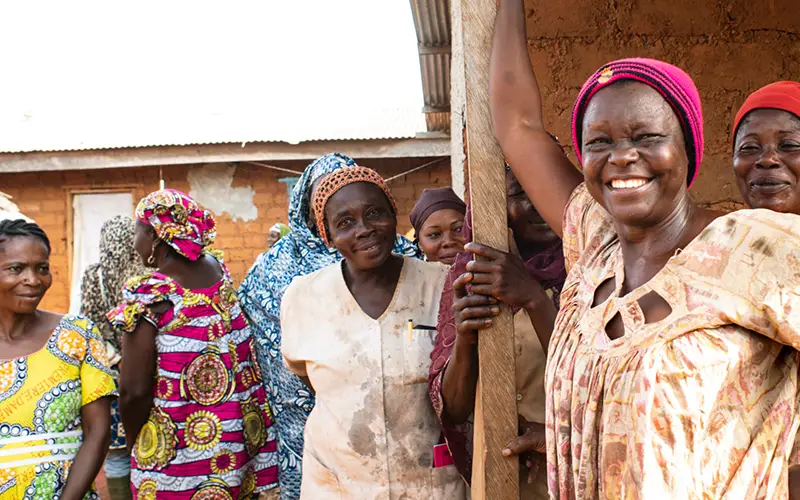 Group of women in colorful clothing and headwraps, smiling outside a building, embodying Cuso International Cameroon.