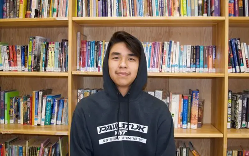 Person in a dark hoodie stands before bookshelves filled with books, evoking the solitude of the Northwest Territories.