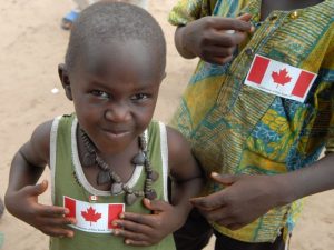 A young child smiling at the camera wearing a Canada flag sticker