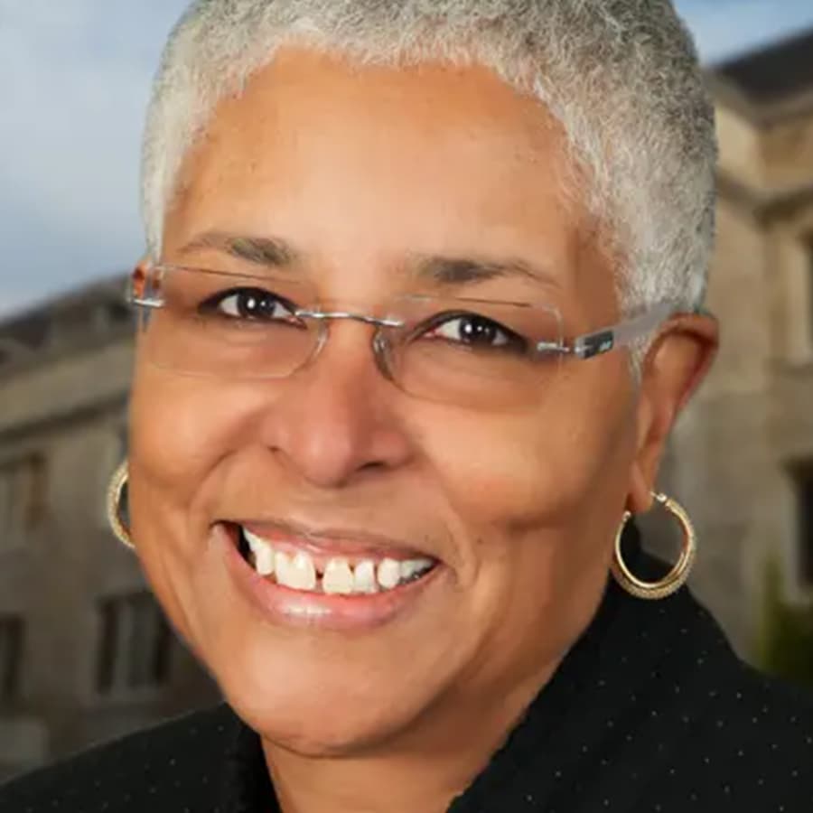 A Black woman with grey hair and glasses smiling at the camera