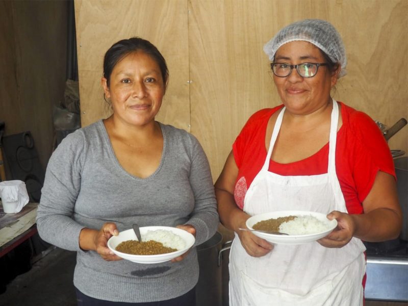 Two Peruvian woman smiling at the camera and holding plates of food