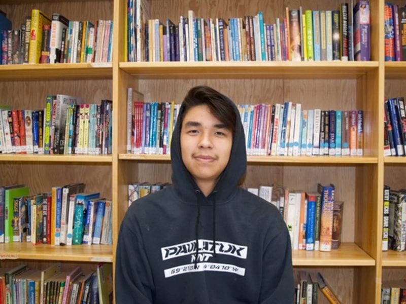A young man in a hoodie standing in front of a book shelf