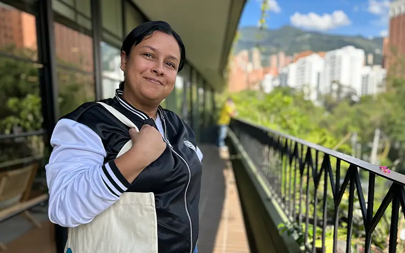 Person smiling, holding a bag on a balcony in Colombia with cityscape and mountains, working with Cuso International.