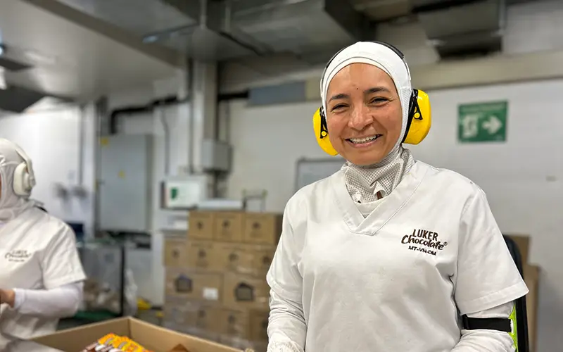 Smiling worker in a white uniform and yellow ear protection at the Cuso International Colombia chocolate factory.