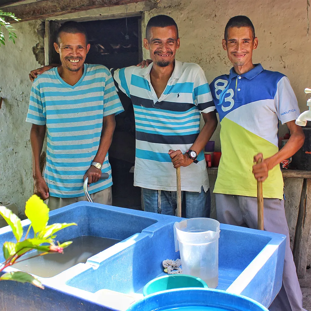 Three men smiling beside a blue water tank setup outdoors.