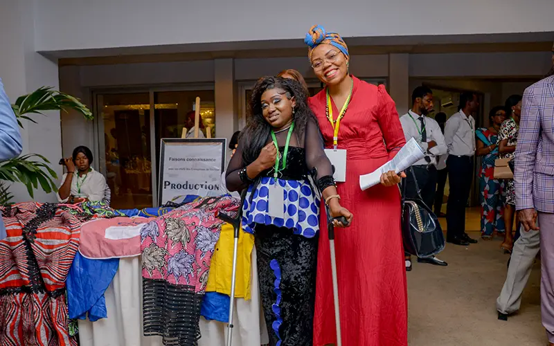 At an indoor event, two women pose near vibrant fabric displays, promoting Cuso International in the DRC.