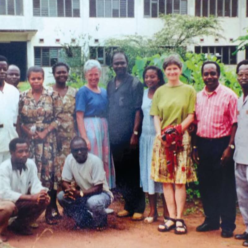 A group of men and women standing in front of a white building with lush green pants