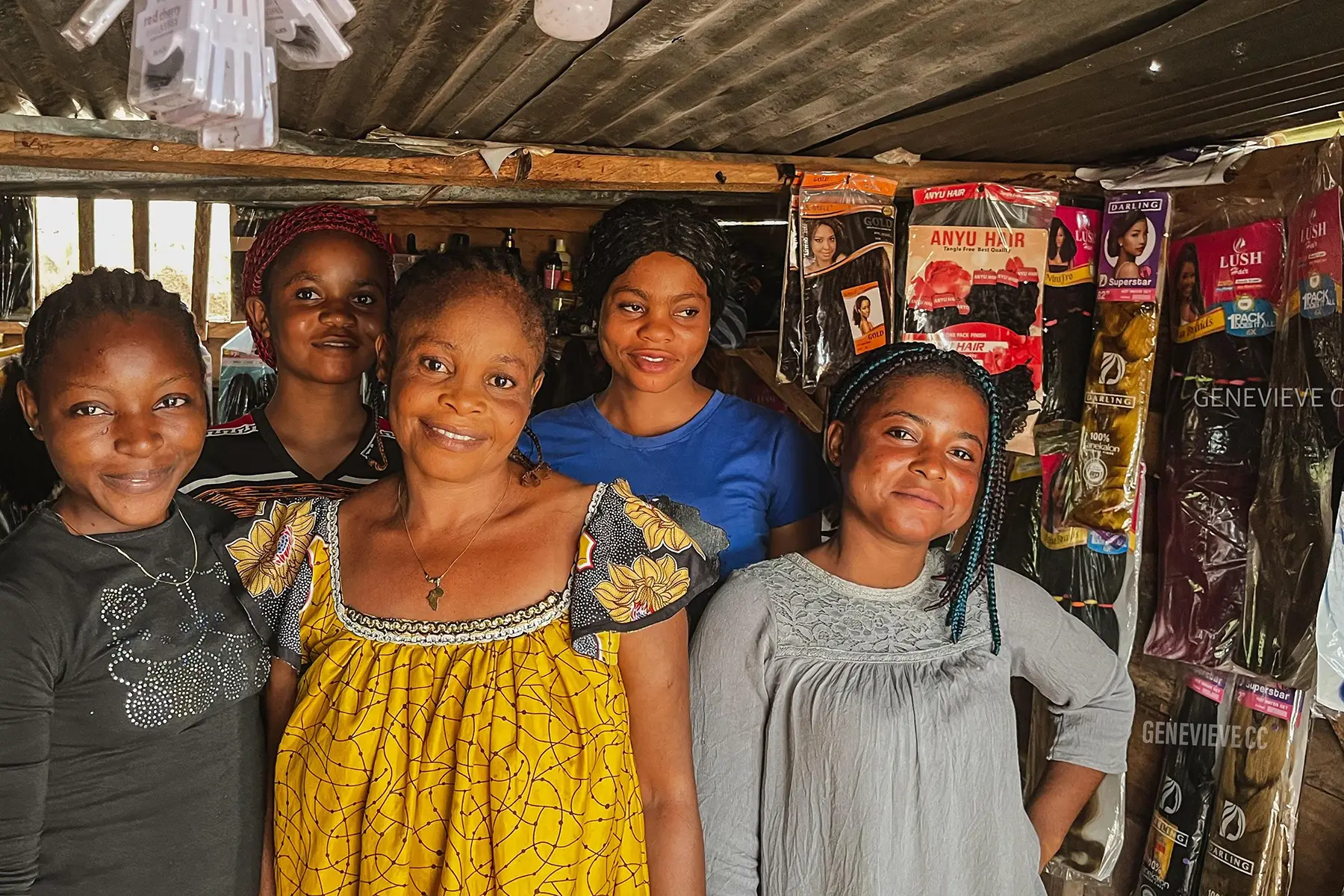 Five smiling people stand in Cuso International Nigeria's shop, surrounded by hair product packaging on the walls.