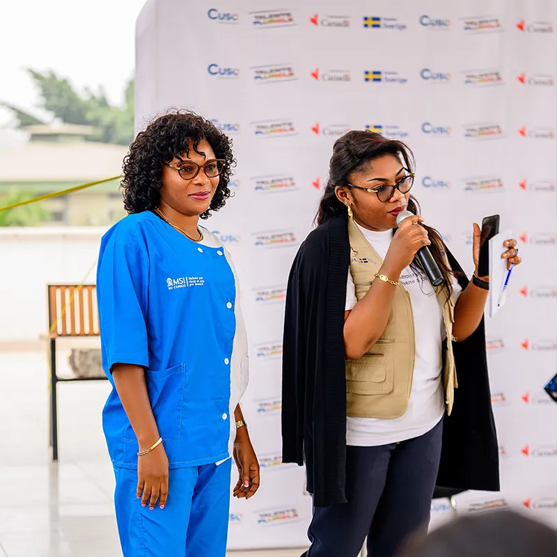 Two women presenting at a branded event backdrop / Deux femmes présentant devant un fond d’événement