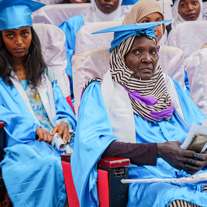 Diplômée âgée en toge bleue assise et regardant la caméra